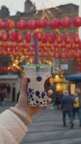 Vertikales-Video-Nahaufnahme-Einer-Hand-Mit-Bubble-Tea-Zum-Mitnehmen-In-Chinatown,-London,-Großbritannien